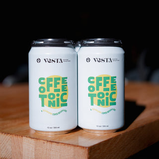 Two cans of Vesta Coffee & Tonic on a wooden surface with a dark background